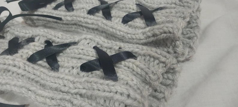 May include: Gray knitted fabric with black ribbon crisscrossing the fabric. The fabric is soft and textured.