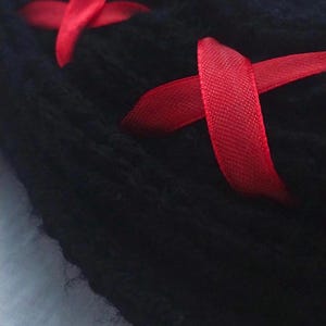 May include: Black fabric with red ribbon tied in a criss-cross pattern. The fabric is soft and fuzzy.