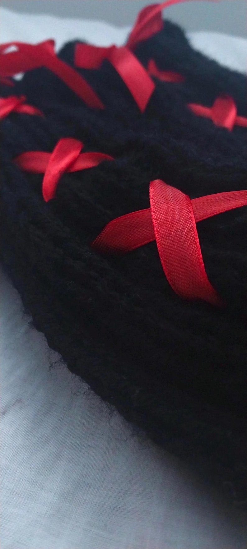 May include: Black fabric with red ribbon tied in a criss-cross pattern. The fabric is soft and fuzzy.
