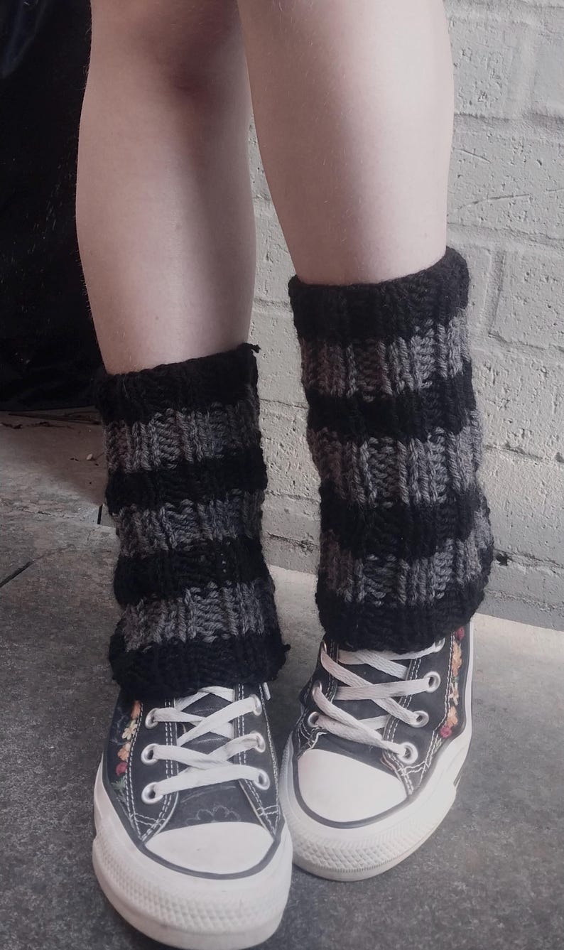 May include: A pair of black and gray striped leg warmers worn with black canvas high-top sneakers with floral embroidery.