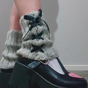 May include: Gray knitted leg warmers with black ribbon laces and a pair of black platform shoes with a pink heart detail.
