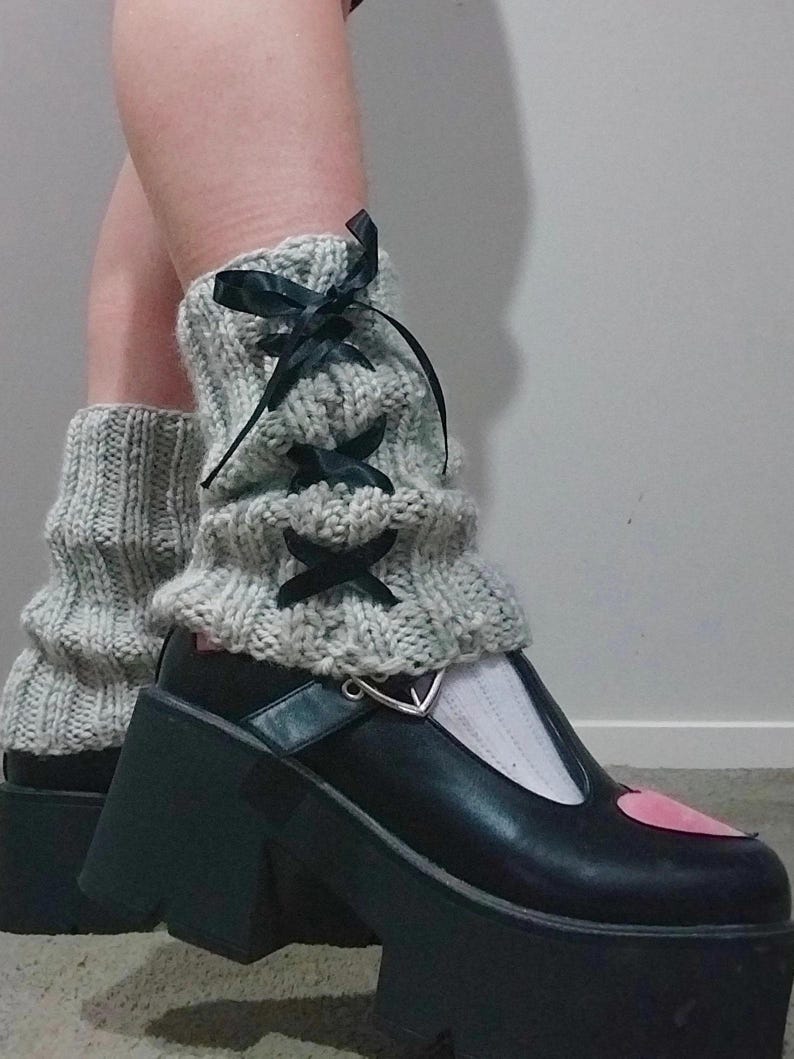 May include: Gray knitted leg warmers with black ribbon laces and a pair of black platform shoes with a pink heart detail.