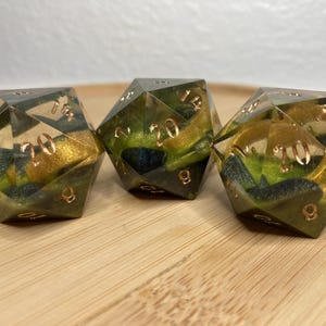 May include: Three green, gold, and black resin dice with numbers 1-20 on each face. The dice are clear and show the numbers through the resin.