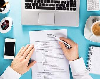 May include: A person reviewing a resume on a blue desk with a laptop, coffee, and a notepad. The resume has the heading "RESUME" and lists "SUMMARY", "WORK EXPERIENCE", and "ACADEMIC QUALIFICATIONS".