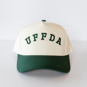 May include: A white baseball cap with a green brim and the word "UFFDA" embroidered in green on the front.