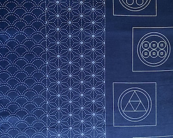 May include: A dark blue fabric with white stitching in geometric patterns. The fabric features four squares with white stitching of different symbols, including a circle with three dots, a circle with eight dots, a triangle within a circle, and a bird within a circle.