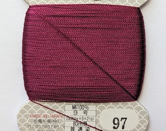 May include: A spool of burgundy silk thread with a gold label. The label reads "絹100% 9号 23tex×9×2(s) 80m巻 普通染 絹手縫糸 97" and "金亀糸業(株) MADE IN JAPAN".