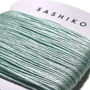May include: A spool of light green sashiko thread, a type of Japanese embroidery thread, with the word "SASHIKO" printed on the label. The label also indicates that the thread is 100% cotton and 30 meters long.