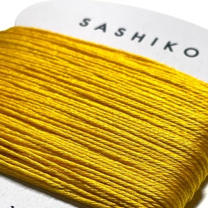 May include: A spool of bright yellow sashiko thread, 100% cotton, with the text "SASHIKO" and "30m" printed on the label.