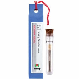 May include: A glass tube filled with assorted sewing needles, labeled "Tulip Sewing Needles" and "Hiroshima Needles". The tube is topped with a cork stopper and has a red string attached to the top.