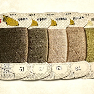 May include: Spools of silk thread in shades of brown and green, labeled with numbers 61 through 65. Each spool is labeled with Japanese text and a gold turtle logo. The thread is 100% silk.