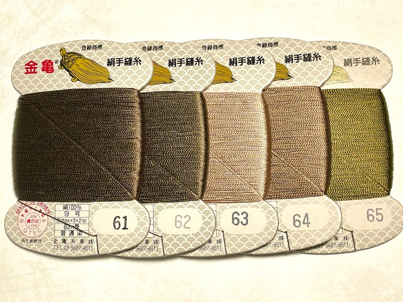 May include: Spools of silk thread in shades of brown and green, labeled with numbers 61 through 65. Each spool is labeled with Japanese text and a gold turtle logo. The thread is 100% silk.