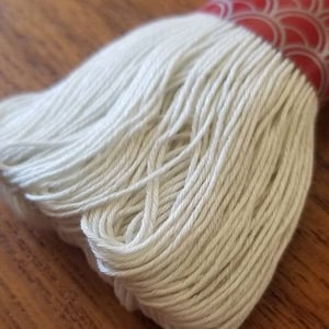 May include: A close-up of a spool of white embroidery floss. The floss is wound tightly and has a smooth, even texture.