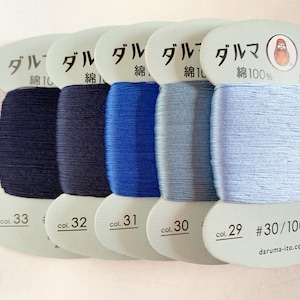 Op de afbeelding: Vijf spoelen blauwe katoenen draad, gelabeld met het Japanse woord "ダルマ" (Daruma) en de tekst "綿100%" (katoen 100%). De spoelen zijn genummerd 33, 32, 31, 30 en 29. De laatste spoel heeft ook de tekst "#30/100m" en "daruma-ito.co.jp".