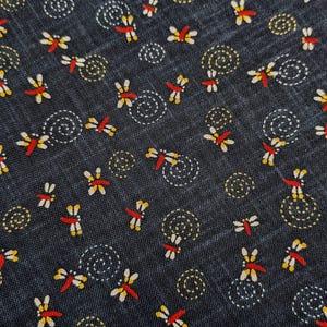 May include: Dark blue fabric with a repeating pattern of dragonflies in red, yellow, and white. The design includes spiral and circular accents in white and yellow, creating a textured appearance.