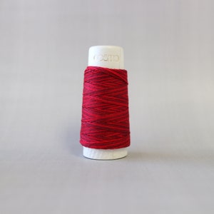 May include: A spool of red and dark red embroidery thread wound on a white plastic bobbin. The bobbin is labeled "cosmo".
