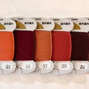 May include: A collection of six spools of thread in various shades of brown, ranging from light orange to dark brown. Each spool is labeled with a number from 35 to 40. The packaging includes Japanese text and a gold turtle logo.