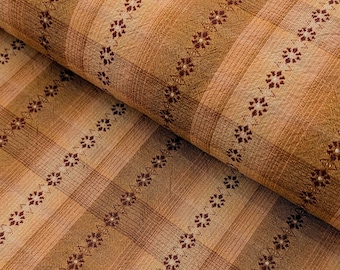 May include: Close-up of a folded fabric with a plaid pattern in shades of tan, brown, and peach. The fabric features rows of small, dark red floral designs. The texture appears soft and slightly textured, suitable for various textile projects.