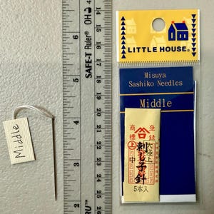 Pu&ograve; includere: Un pacchetto di aghi Sashiko Misuya etichettato "Medio". La confezione &egrave; blu e bianca con un piccolo logo di una casa e il testo "Little House". Gli aghi sono confezionati in una piccola busta bianca con testo giapponese.