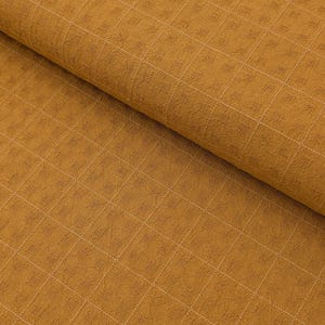 May include: Close-up of a textured fabric in a warm mustard yellow hue. The fabric features a grid pattern created by subtle, raised squares and delicate white stitching. The material is folded, showing depth and texture.