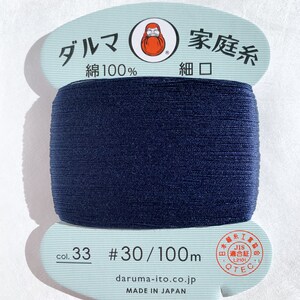 May include: A spool of dark blue thread labeled "Daruma Family Thread, Cotton 100%, Fine Mouth, Col. 33 #30/100m, daruma-ito.co.jp, Made in Japan". The spool has a red and white label with a cartoon image of a man with a beard.