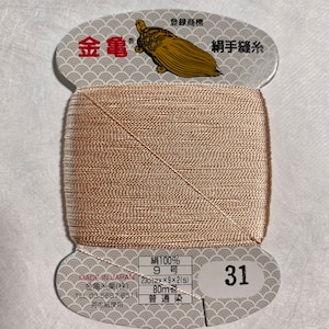 May include: A spool of beige silk thread with a label that reads "Silk 100%, 9 号, 230m x 9 x 2(s), 80m, 普通染, 31". The label also includes the text "金亀糸業(株), MADE IN JAPAN, TEL 03-5687-8511, 再生紙使用".