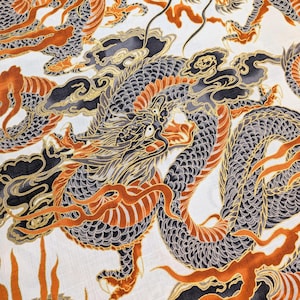 May include: White fabric with a repeating pattern of stylized dragons. The dragons are primarily gray with orange and gold accents. Black cloud-like shapes and orange flame-like designs are also present.