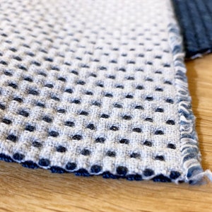 May include: Close-up of a gray and blue fabric with a textured, waffle-like pattern. The fabric has a dark blue border.