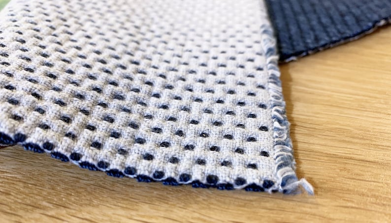 May include: Close-up of a gray and blue fabric with a textured, waffle-like pattern. The fabric has a dark blue border.
