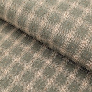 May include: Close-up of a fabric with a plaid pattern. The fabric features a grid of light beige and sage green squares and lines. Small, dark brown dots are scattered throughout the design. The fabric is folded, showing its texture and depth.