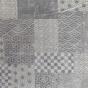 May include: A close-up of a textile with a patchwork design in shades of gray. The pattern includes geometric shapes, such as squares, circles, and starbursts, creating a textured surface. The fabric appears to be woven.