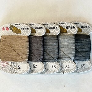May include: Five spools of thread in varying shades of brown and gray, labeled 51 through 55. Each spool is neatly wound and attached to a decorative label with Japanese text and a gold emblem. The thread is likely for sewing or embroidery.