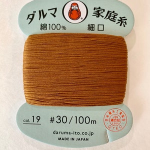 May include: A spool of brown thread labeled "Daruma Family Thread, Cotton 100%, Fine Mouth, Col. 19 #30/100m, daruma-ito.co.jp, Made in Japan". The label also features a red and white illustration of a Japanese Daruma doll.