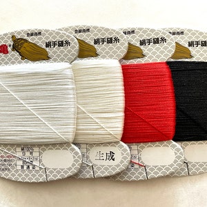May include: Four spools of sewing thread in white, off-white, red, and black. Each spool is labeled with Japanese text and a gold turtle logo. The thread is 80 meters long.