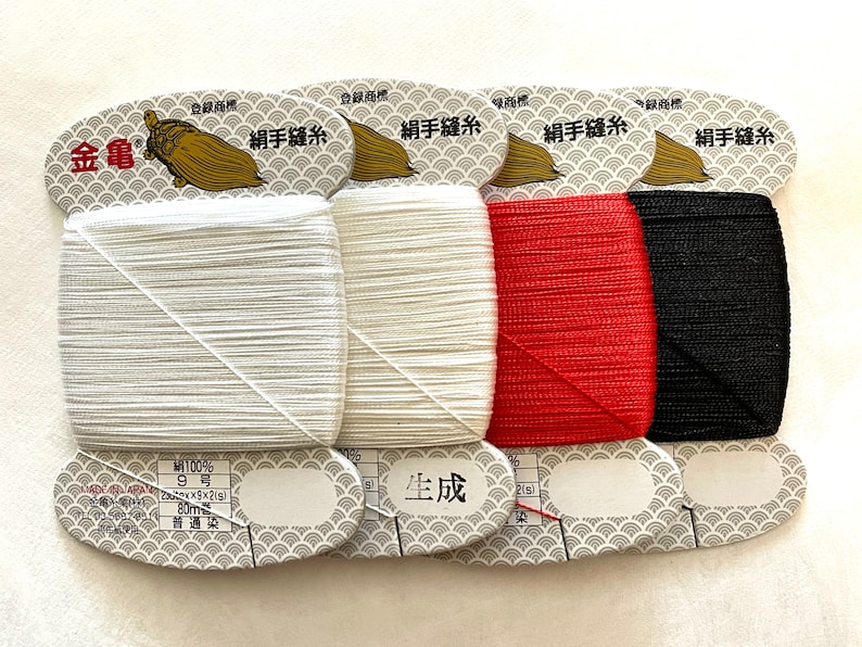 May include: Four spools of sewing thread in white, off-white, red, and black. Each spool is labeled with Japanese text and a gold turtle logo. The thread is 80 meters long.