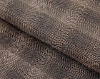 May include: Close-up of a folded fabric with a plaid pattern. The fabric is primarily brown with a subtle grid of lighter beige and orange lines. The texture appears soft and slightly textured, with visible weave details.