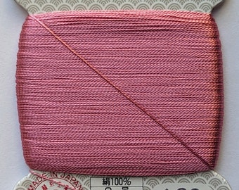 May include: A spool of pink silk thread with a label that reads "絹手縫糸" (silk hand sewing thread) and "金亀" (Kin-Kame) in gold lettering. The label also includes the text "JIS 適合証 L2310 QTEC" and "再生紙使用" (recycled paper used). The spool number is 193.