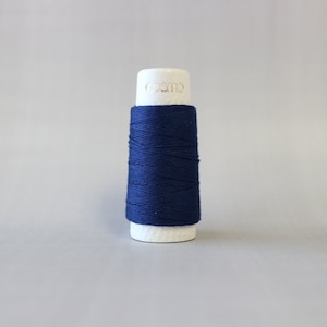 May include: A spool of dark blue thread on a white bobbin with the word "cosmo" printed on the bobbin.