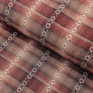 May include: Close-up of a folded fabric with a plaid pattern in shades of burgundy, tan, and brown. The plaid design features vertical and horizontal lines, with a decorative floral stripe running diagonally across the fabric.