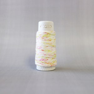 May include: A spool of white thread with pink and yellow speckles. The spool is labeled "cosmo".