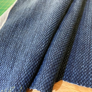 May include: Close-up of a dark blue fabric with a textured, waffle-like pattern. The fabric is folded and has a white border.