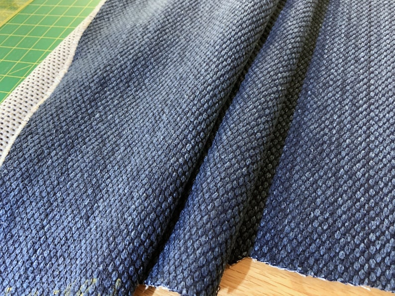 May include: Close-up of a dark blue fabric with a textured, waffle-like pattern. The fabric is folded and has a white border.