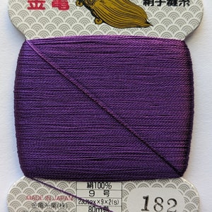 May include: A spool of purple silk thread for hand sewing. The label reads "Made in Japan", "Silk 100%", "9", "23dtex x 9 x 2 (s)", "80m", "Ordinary Dye", "Golden Thread Industry Co., Ltd.", and "182".