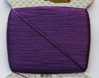 May include: A spool of purple silk thread for hand sewing. The label reads "Made in Japan", "Silk 100%", "9", "23dtex x 9 x 2 (s)", "80m", "Ordinary Dye", "Golden Thread Industry Co., Ltd.", and "182".