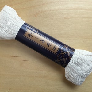 May include: A white spool of thread with a blue and gold label that reads "Sashiko -  糸 (いと)".