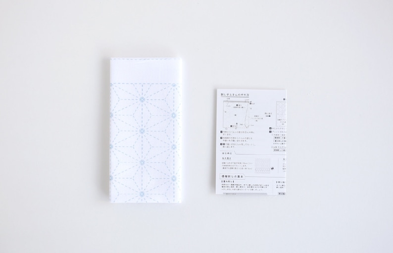 Puede incluir: Una tela blanca con un patr&oacute;n geom&eacute;trico azul, una hoja de instrucciones impresa con texto japon&eacute;s y diagramas para un proyecto de artesan&iacute;a.