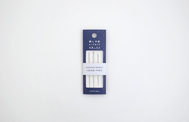 May include: A package of three long sashiko needles in a blue and white cardboard package. The package says "Sashiko Needle Long Type" and "Daruma" on the bottom.