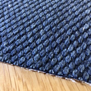 May include: Close-up of a dark blue textured fabric with a raised pattern. The fabric has a slightly fuzzy texture.