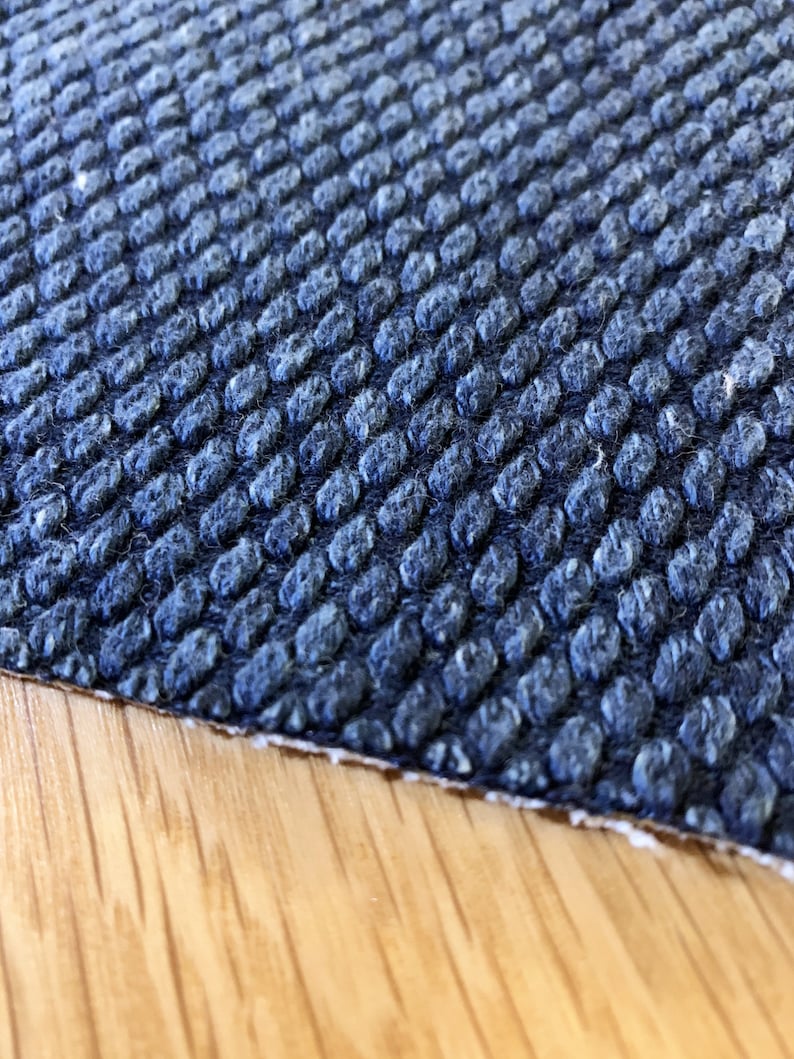 May include: Close-up of a dark blue textured fabric with a raised pattern. The fabric has a slightly fuzzy texture.