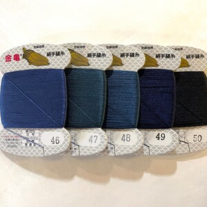 May include: Five spools of thread in shades of blue and black, labeled with numbers 46 through 50. Each spool is rectangular and wrapped in a paper label with Japanese text and a gold logo. The thread is likely for sewing or embroidery.